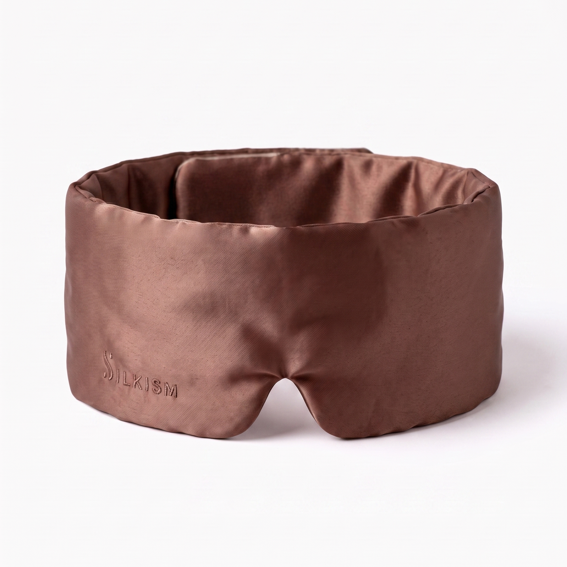 A brown satin sleep mask with a matching padded cushion, shown on a clean white background. The brand name 'Silkism' is subtly debossed on the lower left corner of the mask.