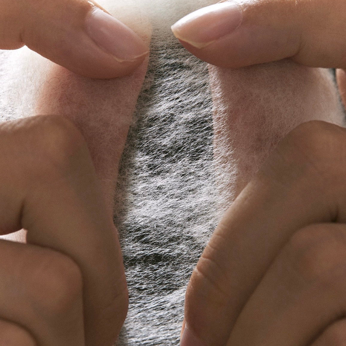 Close-up of a person's hands pulling apart a gray textured fabric or fleece material to show its soft, fuzzy texture.